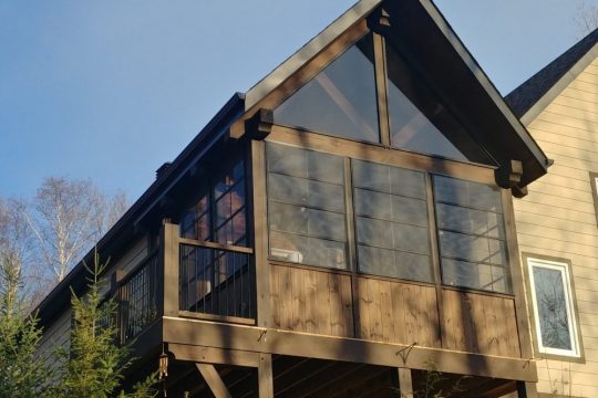 4-track stacking windows enclosing an elevated cabin balcony with a lake and mountain view