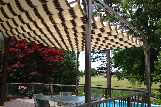 Cream and brown striped retractable canopy gliding along a pergola frame over a poolside deck