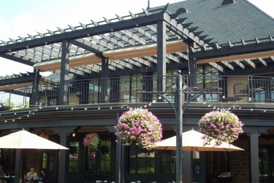 Dark pergola structure with retractable canopy over a restaurant patio