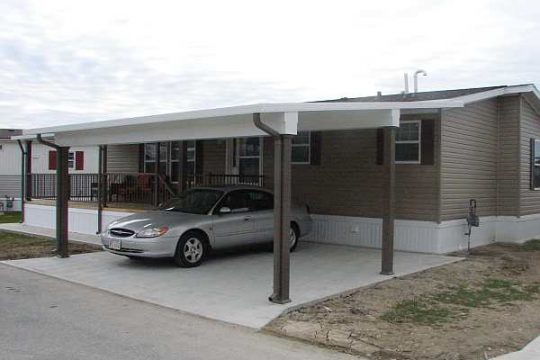 Wide-span PanelCraft insulated roof covering a driveway carport beside a home