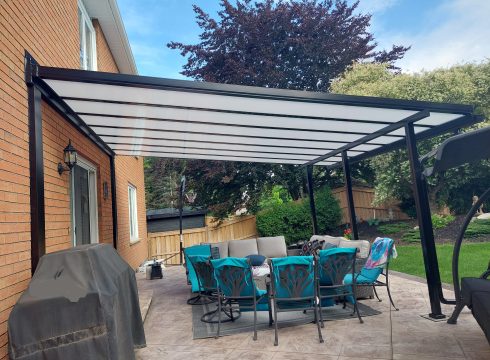 Black-framed Skyview patio cover with polycarbonate roof over a stone patio dining set