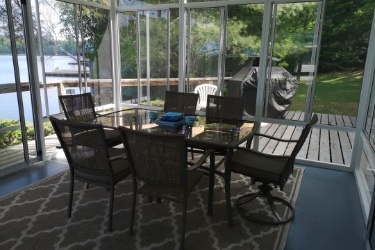 Interior of a lakeside luxury gazebo with a glass-top dining table and screened walls