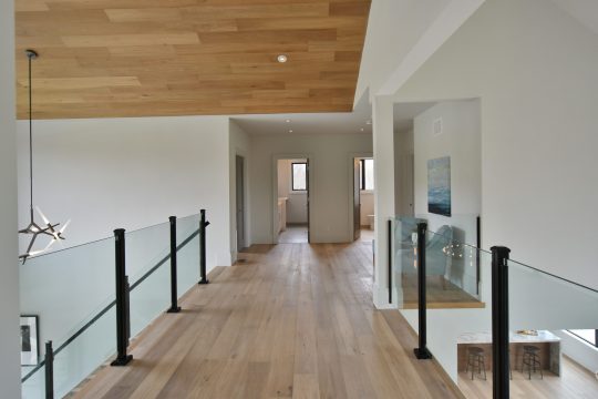 Interior glass railing with slim black posts on a hardwood landing